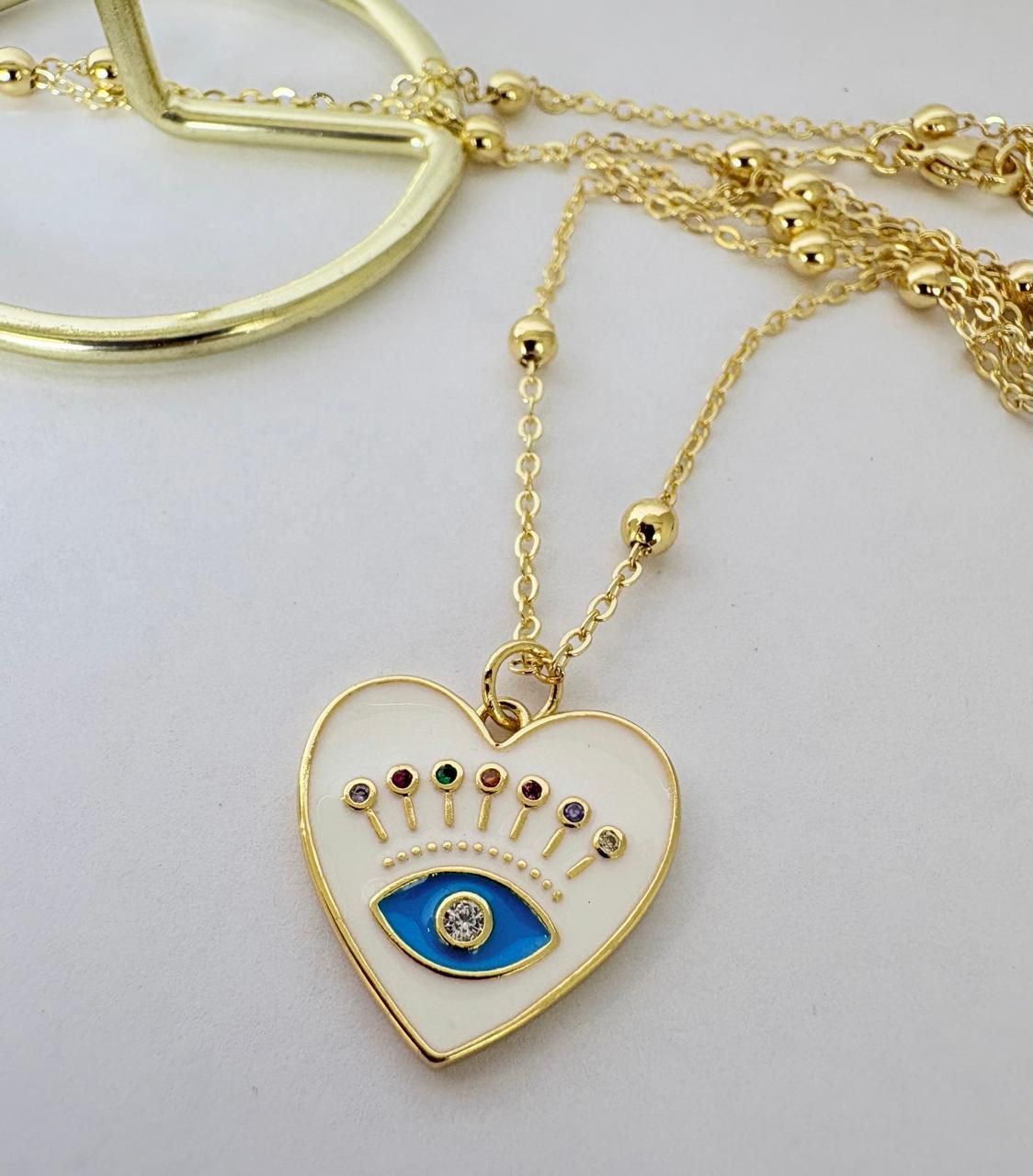 Collar con colgante de corazón dorado, ojo turco azul y pequeñas piedras multicolores sobre fondo blanco