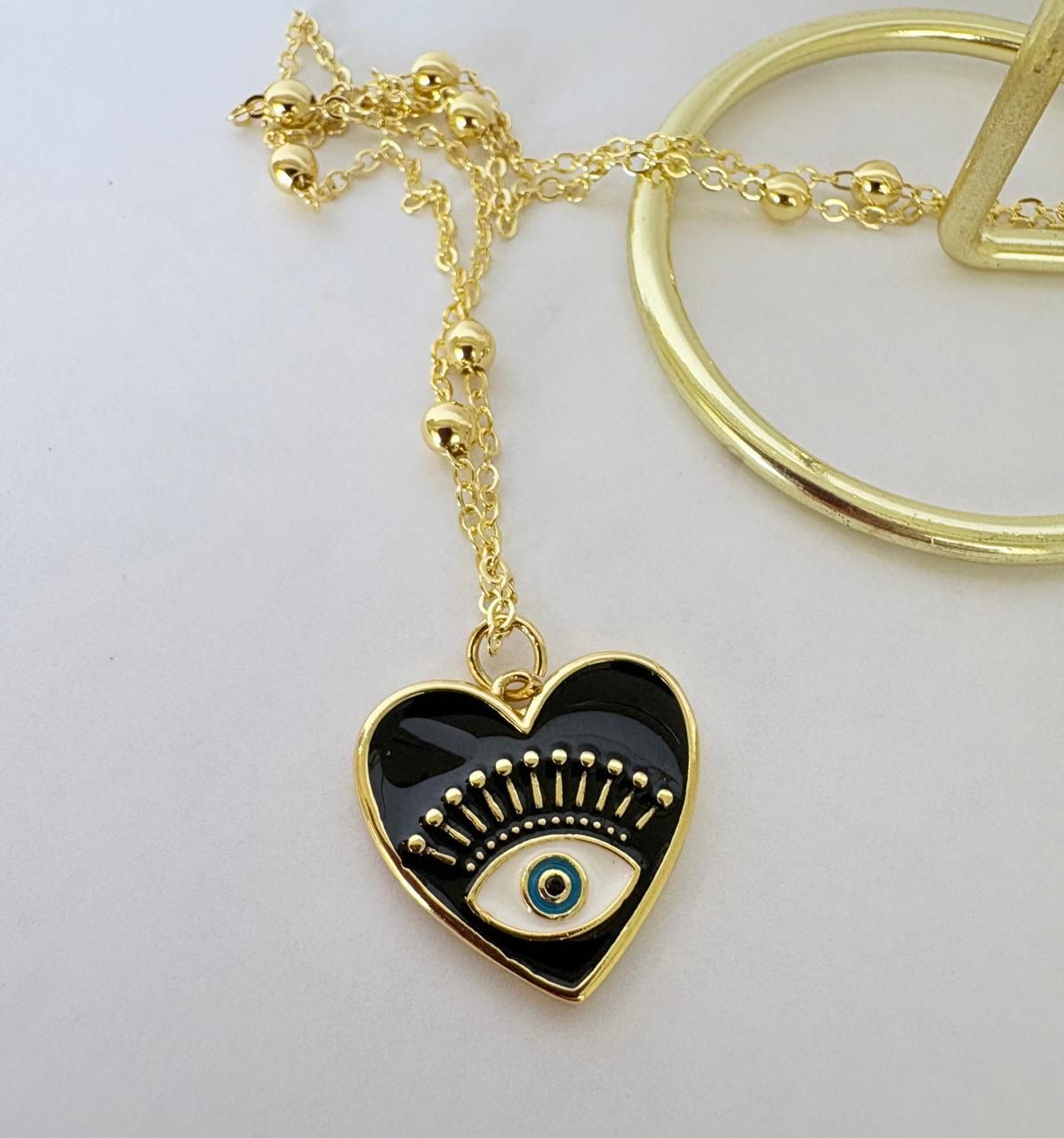 Collar con colgante de corazón dorado, ojo turco azul y pequeñas piedras multicolores sobre fondo blanco