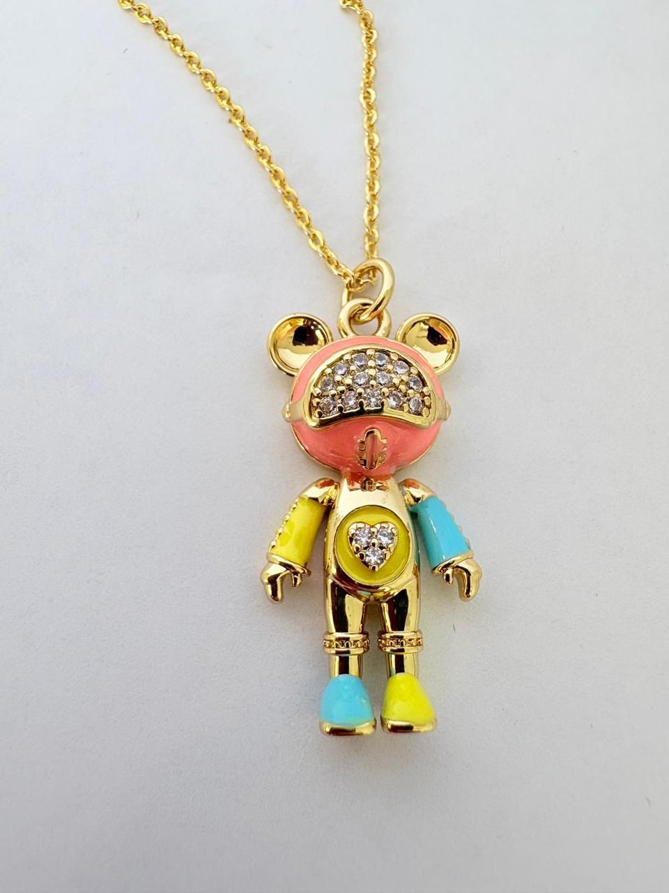 Collar dorado con un colgante de osito de peluche de colores sobre un fondo blanco