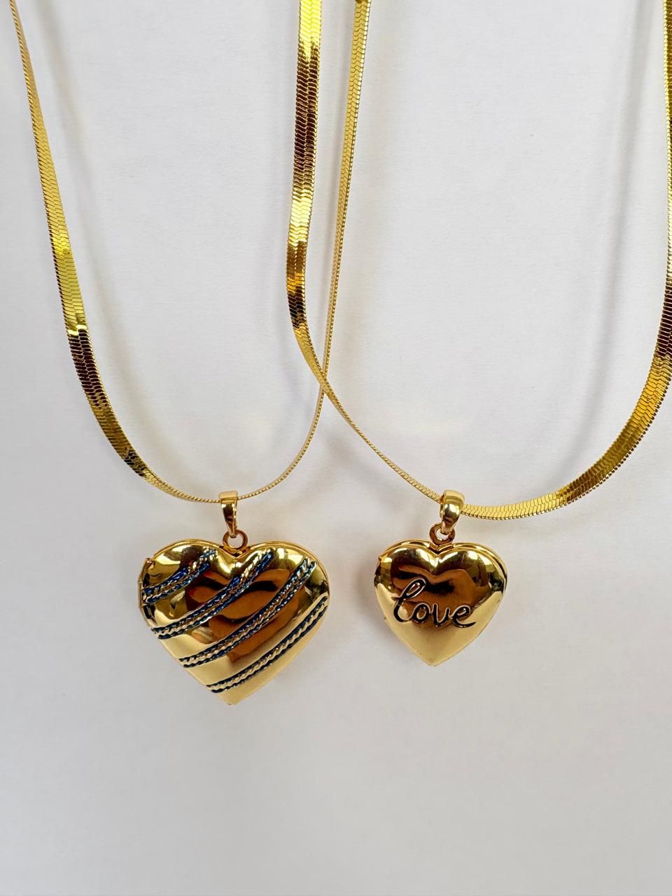 Colgante dorado en forma de corazón con franjas azules, en una fina cadena dorada, sobre un fondo claro