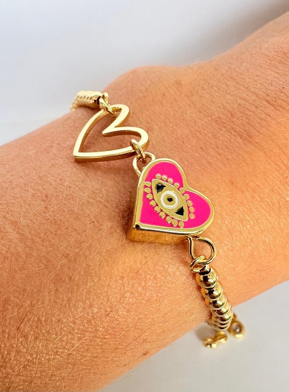 Pulsera dorada con un dije de corazón rosa con un diseño de ojo turco, en una muñeca