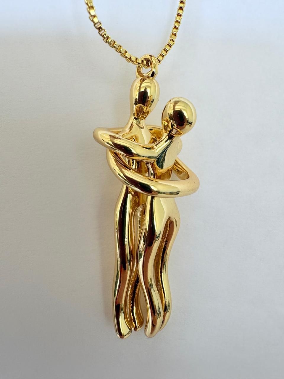 Colgante de oro con dos figuras abstractas abrazadas, en una cadena