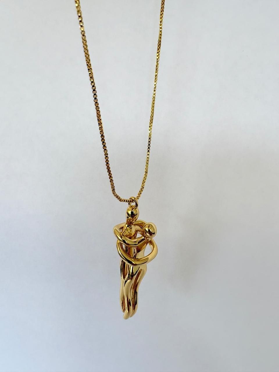 Colgante de oro con dos figuras abstractas abrazadas, en una cadena