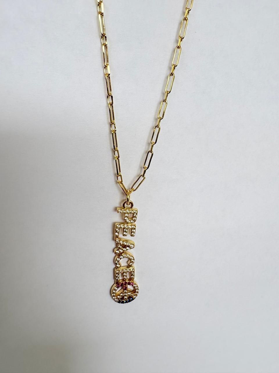 Collar con colgante dorado y un dije alargado sobre un fondo blanco