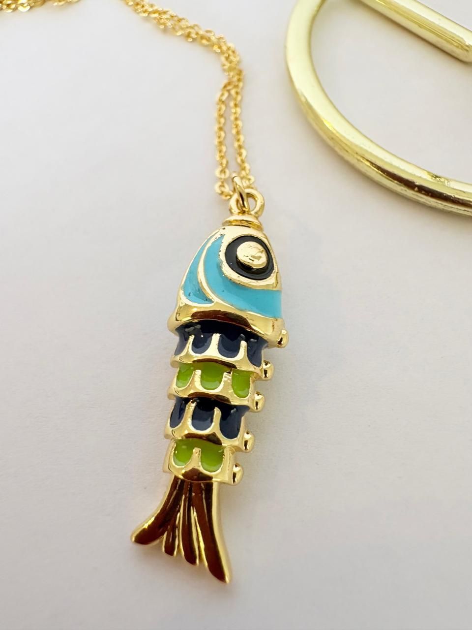 Colgante dorado con forma de pez, con esmalte turquesa y azul oscuro, en una cadena