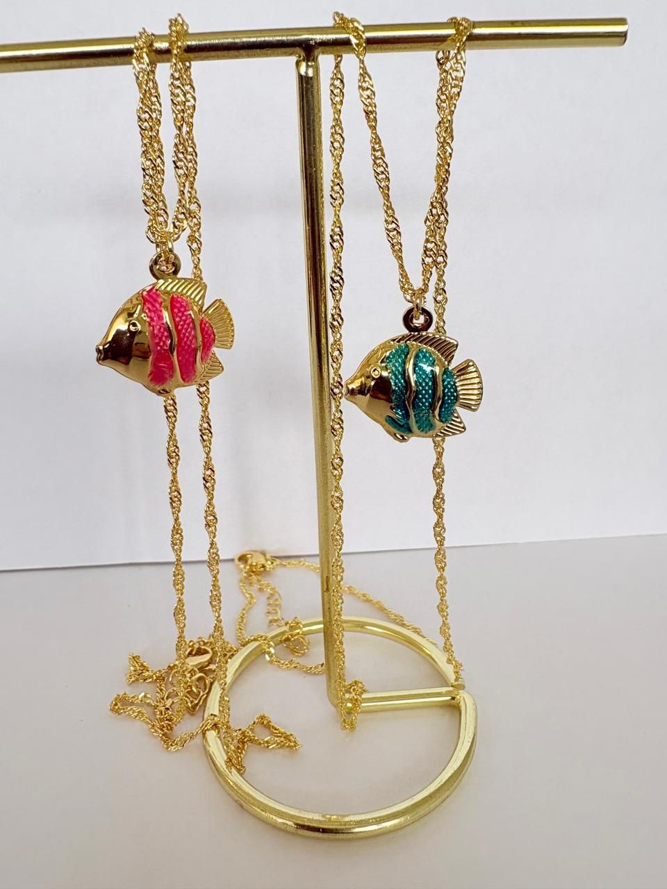 Expositor dorado para joyas con dos collares de colgantes de peces de colores y una pulsera a juego en exhibición