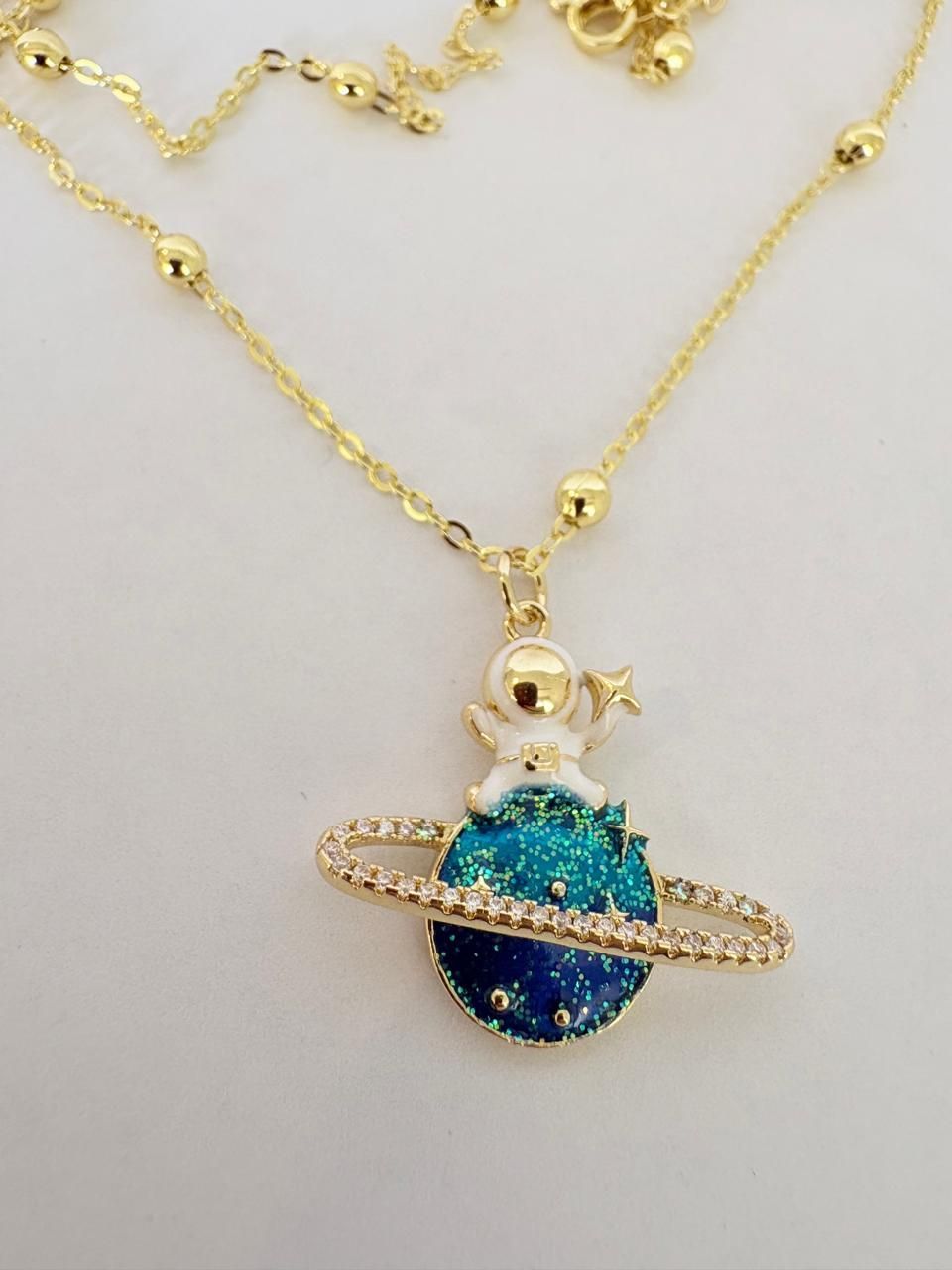 Collar dorado con un colgante de planeta azul y un charm de Saturno con anillos sobre un fondo claro