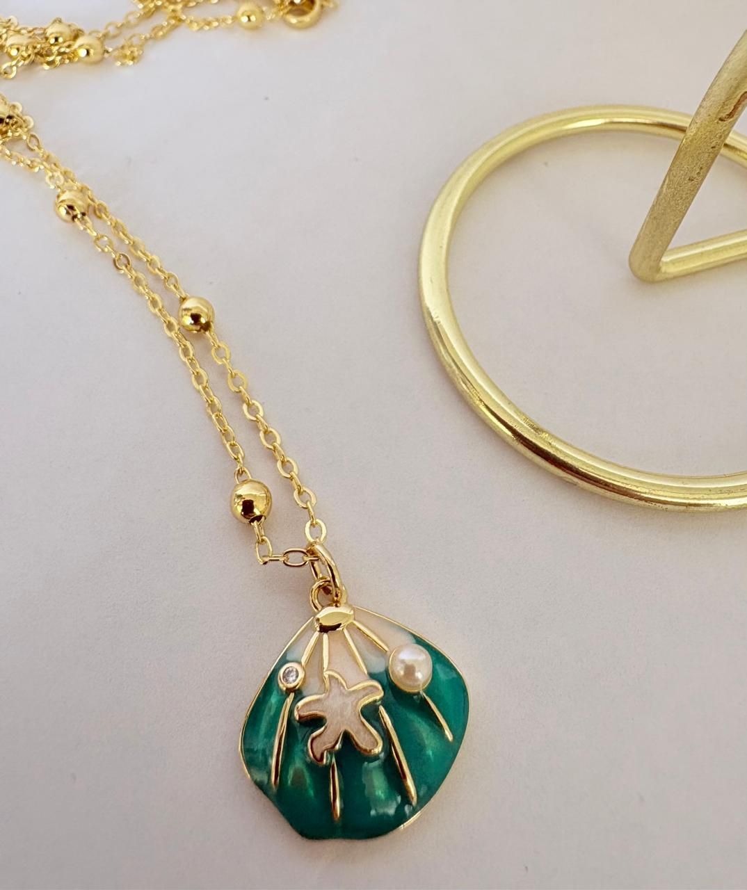 Collar de oro con un colgante de tortuga verde sobre un fondo claro