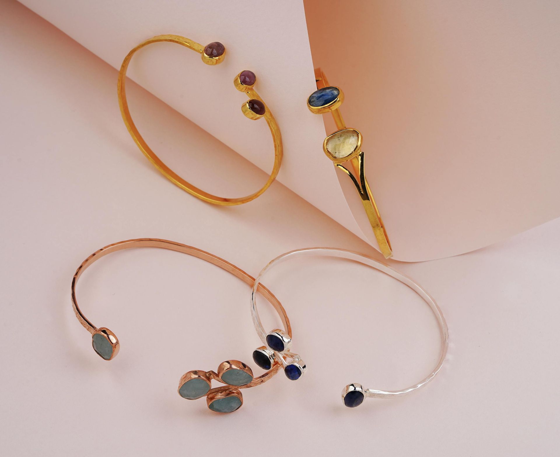 Pulseras de oro y plata con detalles de piedras preciosas azules y moradas sobre un fondo claro