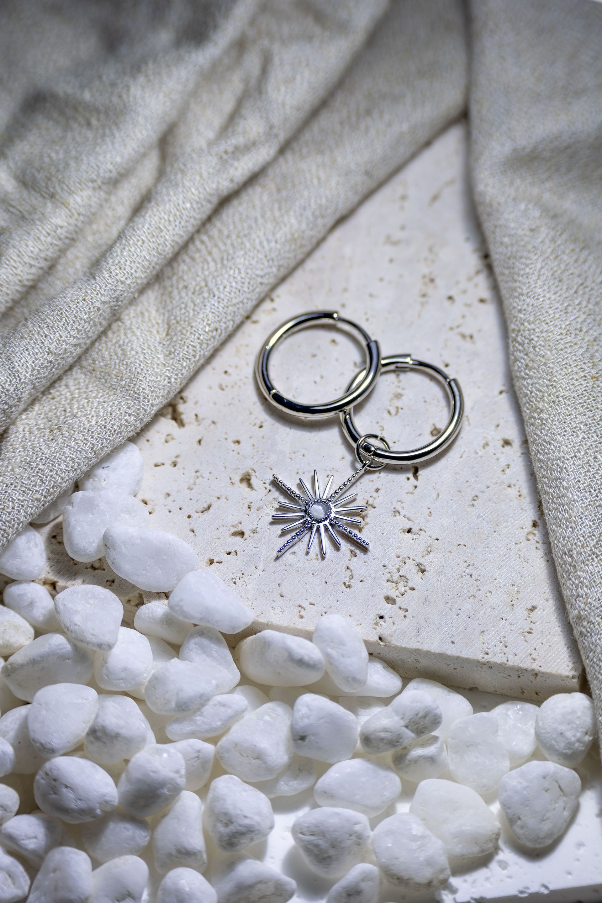 Pendientes de plata sobre una tela blanca, con piedras blancas dispersas y un pequeño colgante con forma de estrella cerca