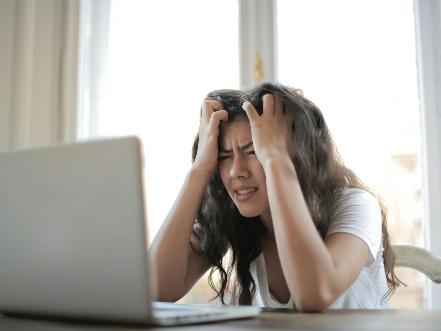 Woman stressed, hands on head, looking at laptop.