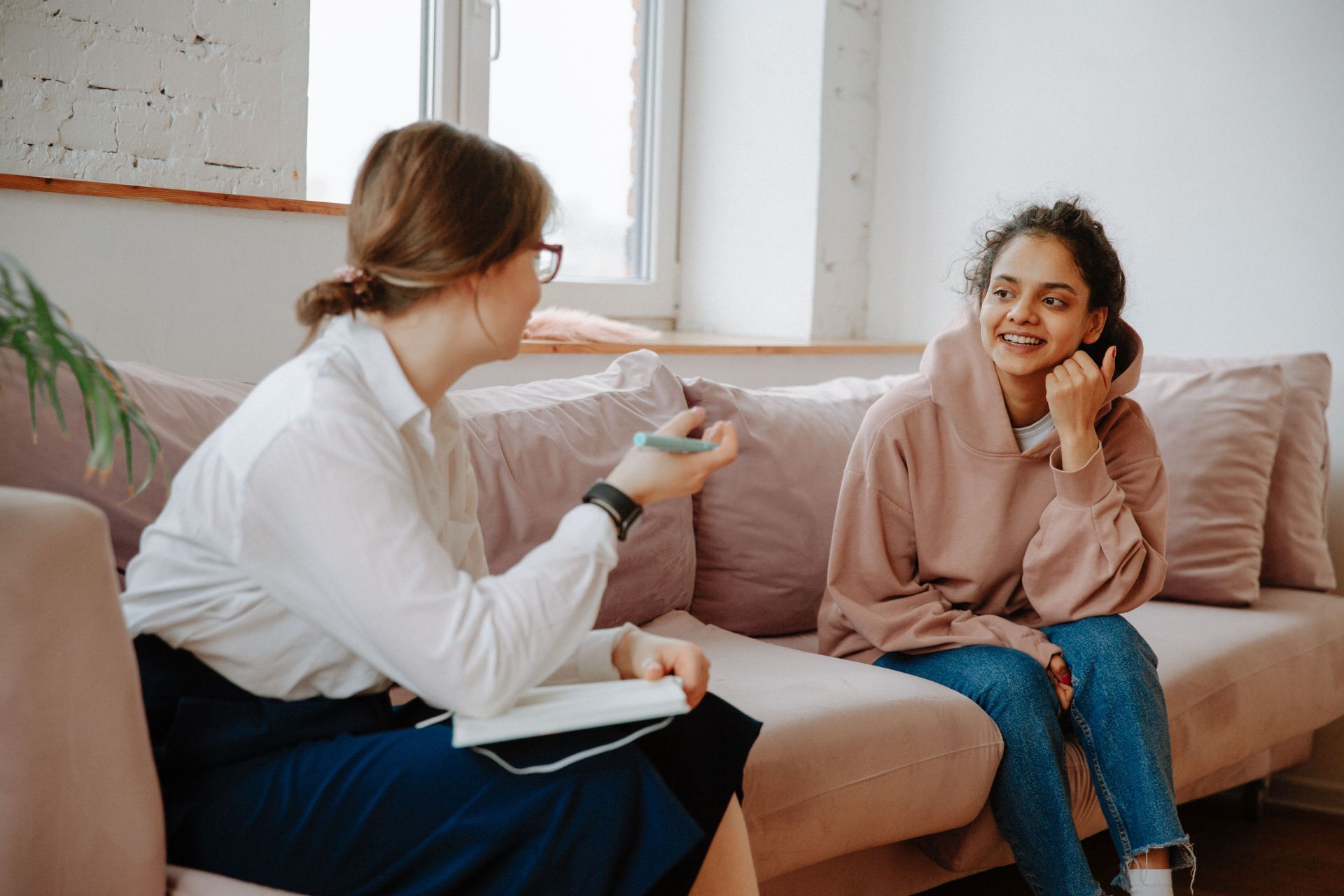 Two individuals, one a therapist and one a young teen, talking on a couch.