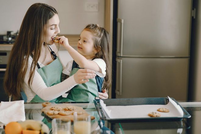Woman and child in aprons baking cookies, child feeding the woman in the kitchen.