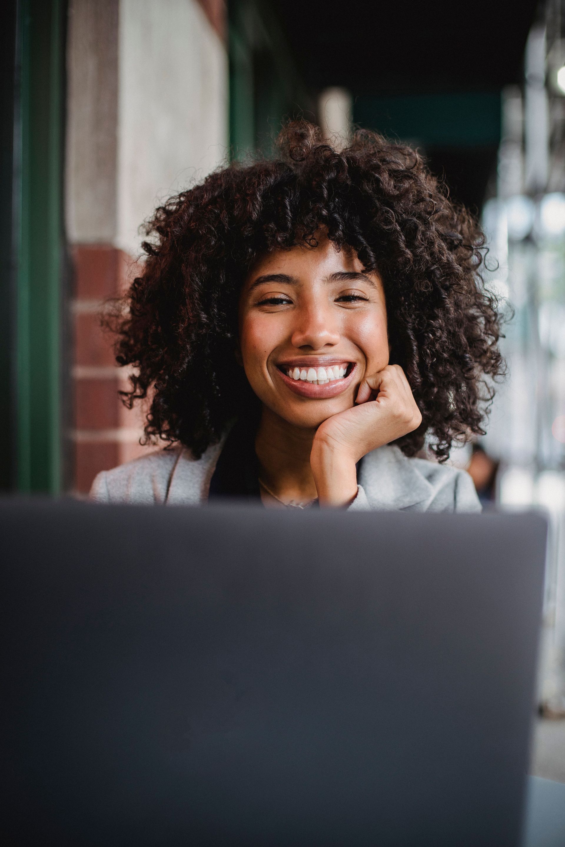Woman smiling behind a laptop at a wooden table in a cozy room