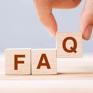 Wooden blocks spelling F, A, Q, with a hand placing the Q on top on a light background