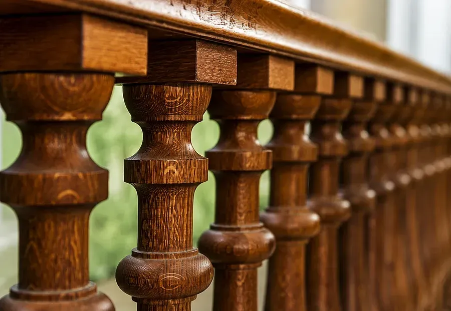 Close-up of a polished wooden railing with carved balusters and a blurred green background