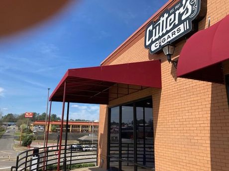 A brick building with a red awning and a sign that says cutter 's cigars