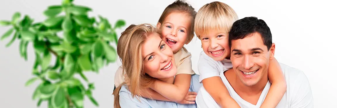A smiling family of four with a plant on the left.