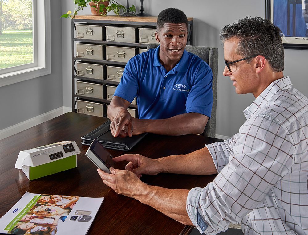 A man in a blue polo and customer in a white shirt reviewing a tablet together at a table.