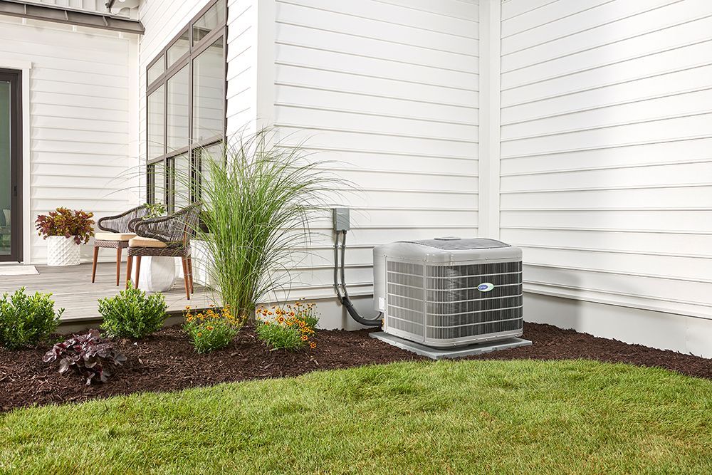 An air conditioning unit sits outside a white house with landscaping.