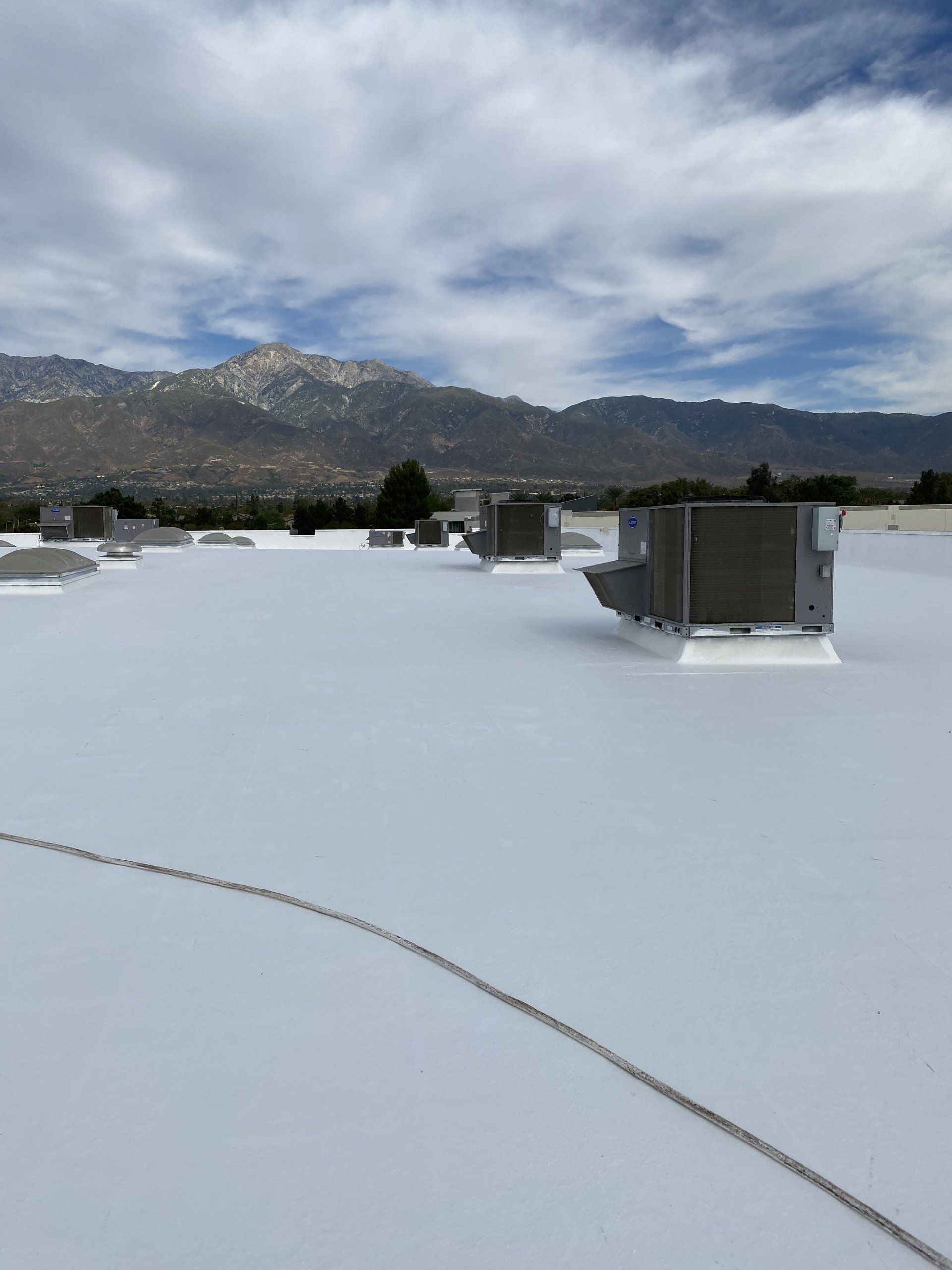 White commercial rooftop with HVAC units, mountains in the background, cloudy sky
