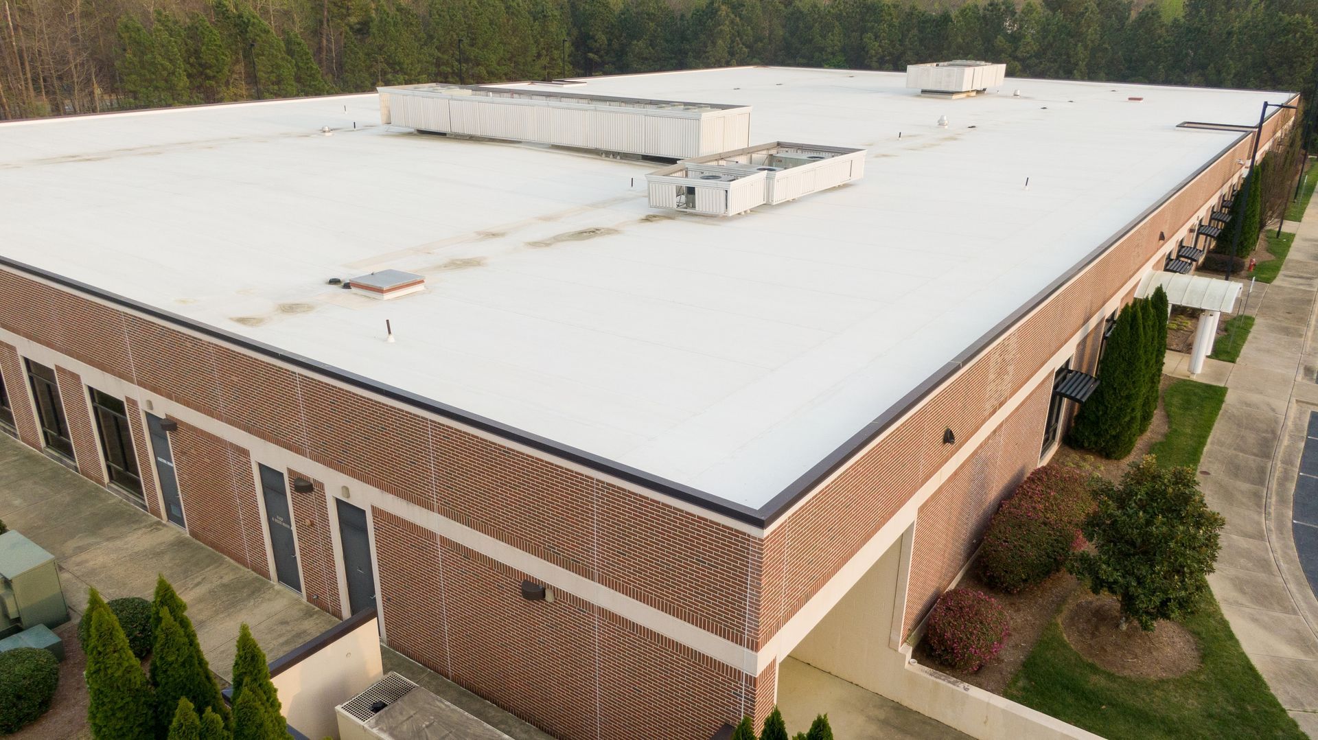 Aerial view of a large white-roofed brick building with trees and sidewalks вокруг it