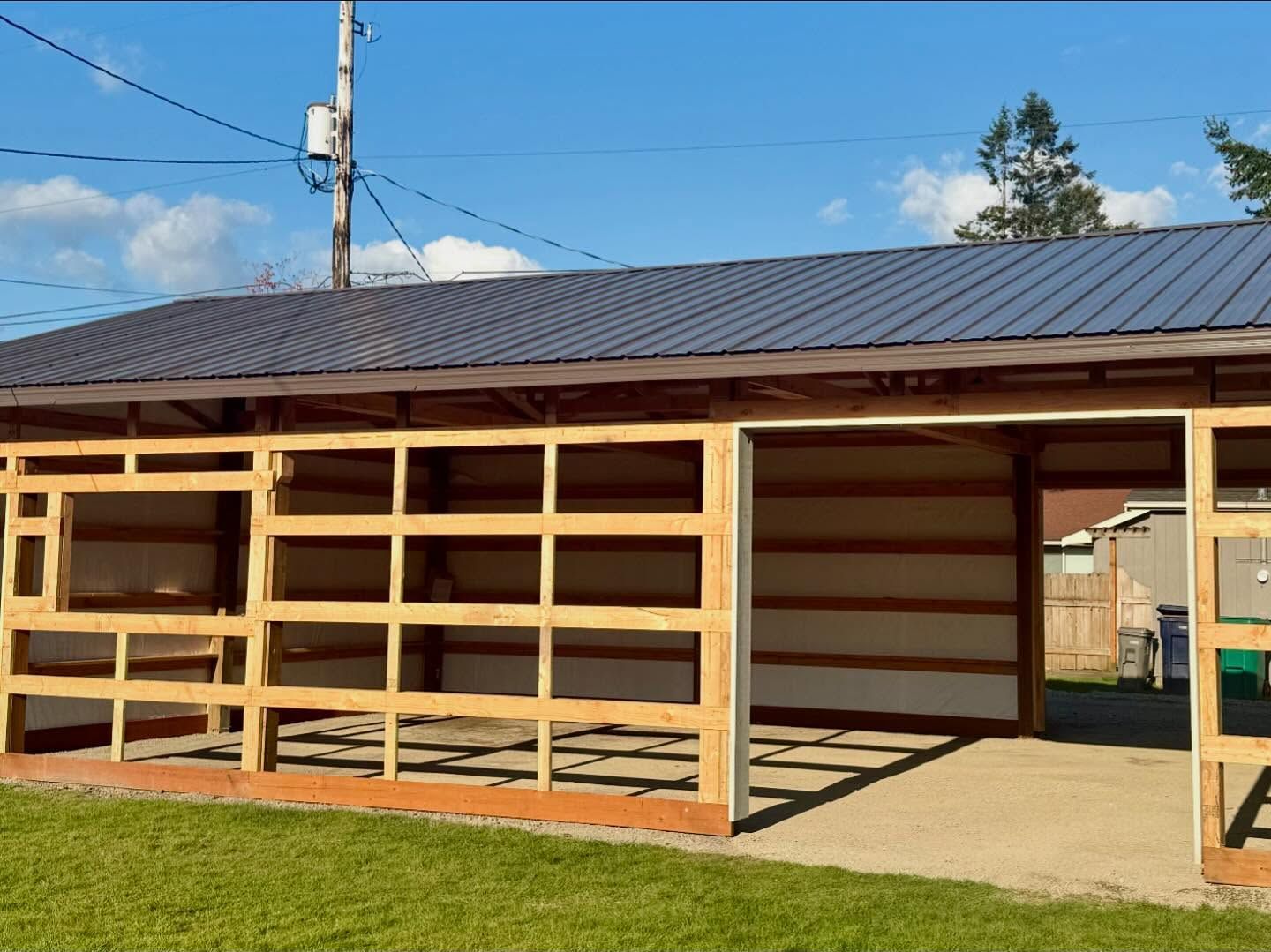 Open wooden porch and covered structure with dark metal roof on a sunny day