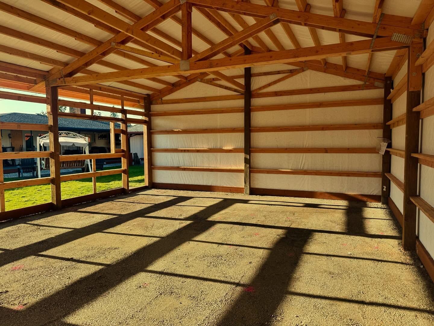 Empty wooden barn interior with sunlit floor and open side views of a green field