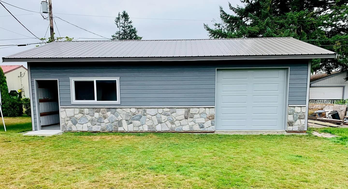 Small gray house with stone base, white garage door, and grassy front yard