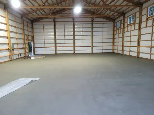 Empty wooden barn interior with sunlit floor and long shadows from the open side.
