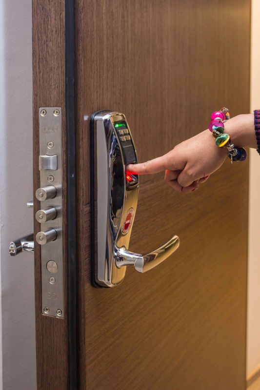 Hand pressing a red keypad on a wooden door lock
