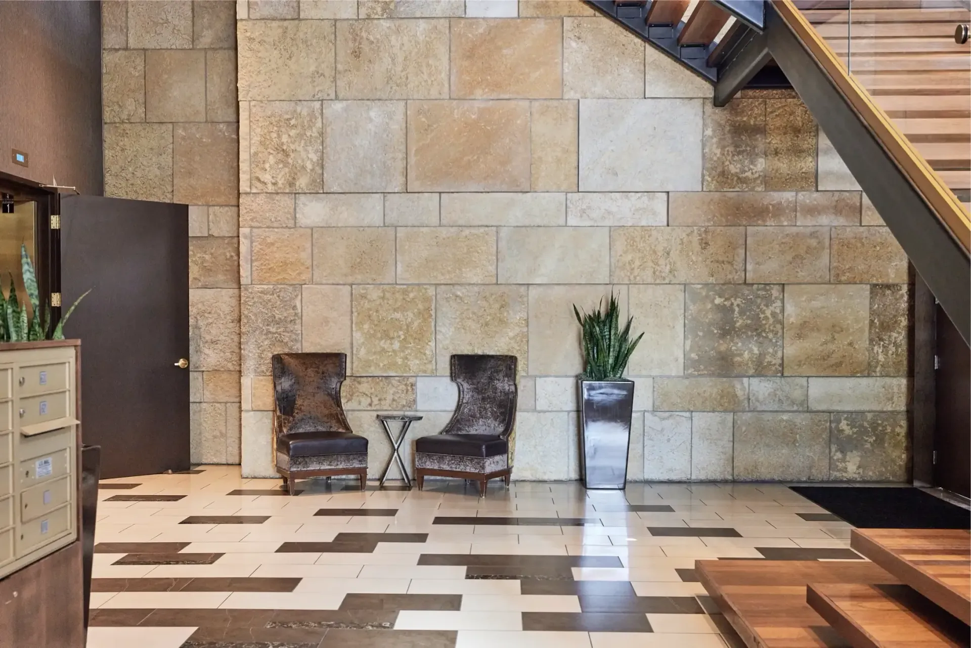 Lobby area with a stone accent wall, two chairs, small table, and plants.