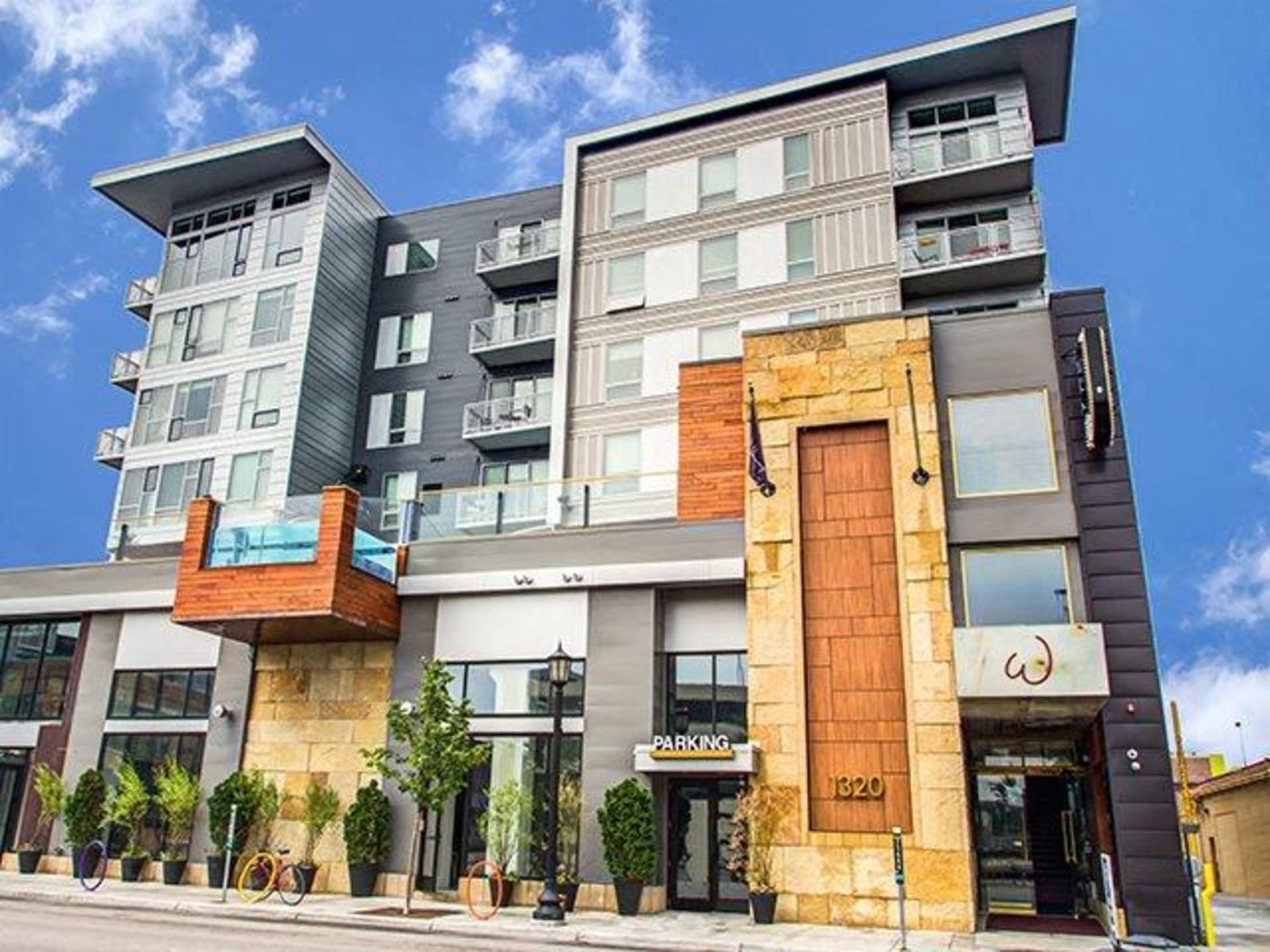 Modern multi-story apartment building exterior with balconies and stone accents against a blue sky.