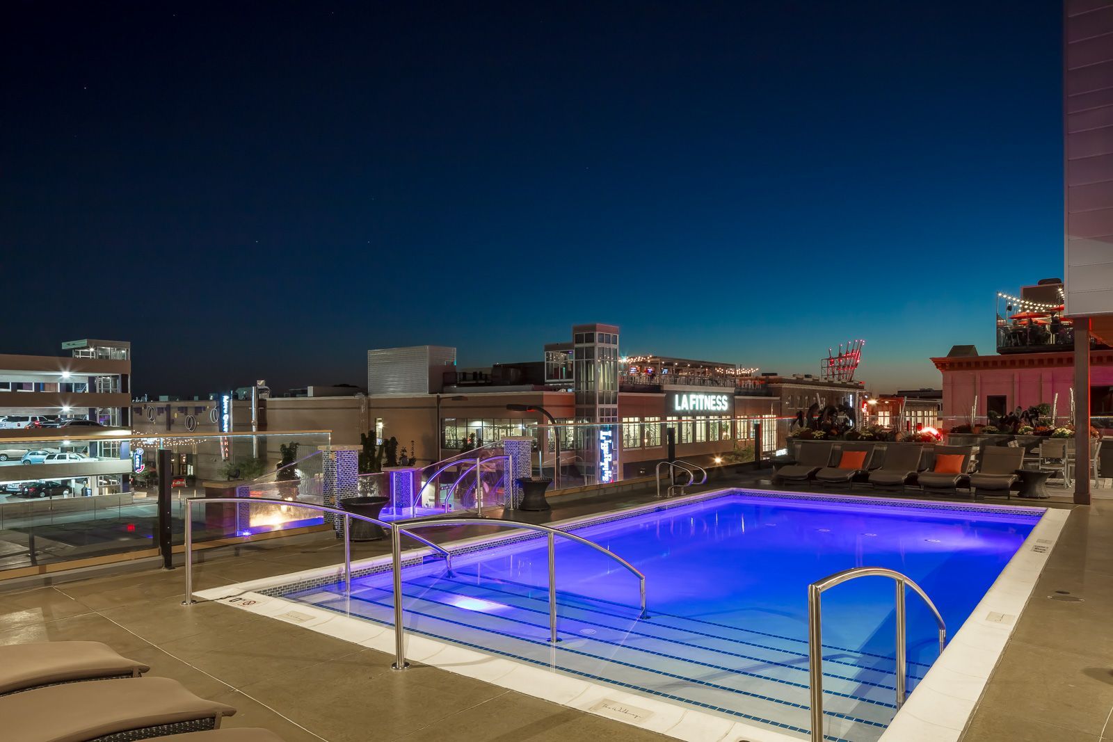 Rooftop pool area at night with lounge chairs and city skyline.