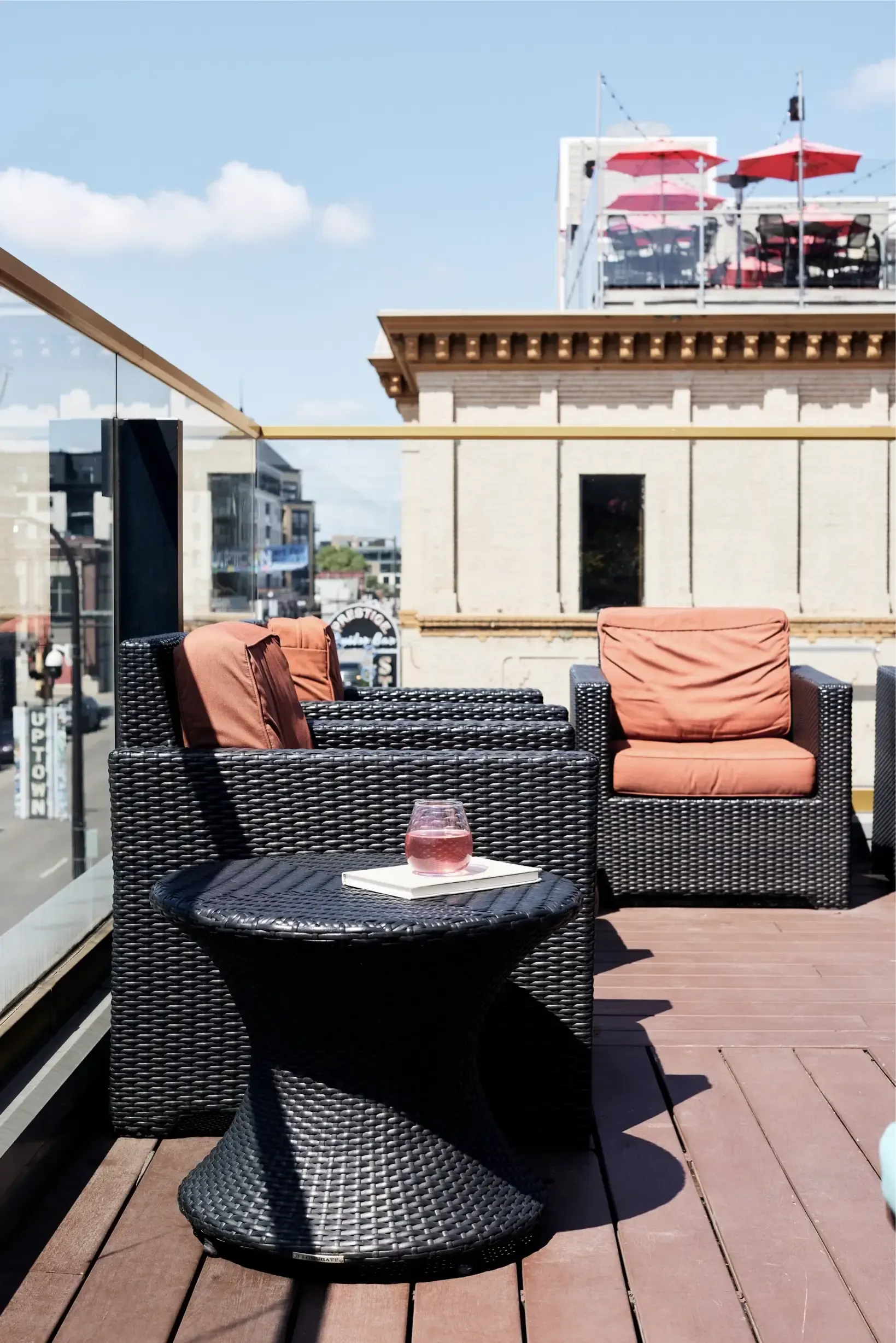 Rooftop outdoor seating on a terrace with wicker chairs and a small table holding a glass, cityscape behind.