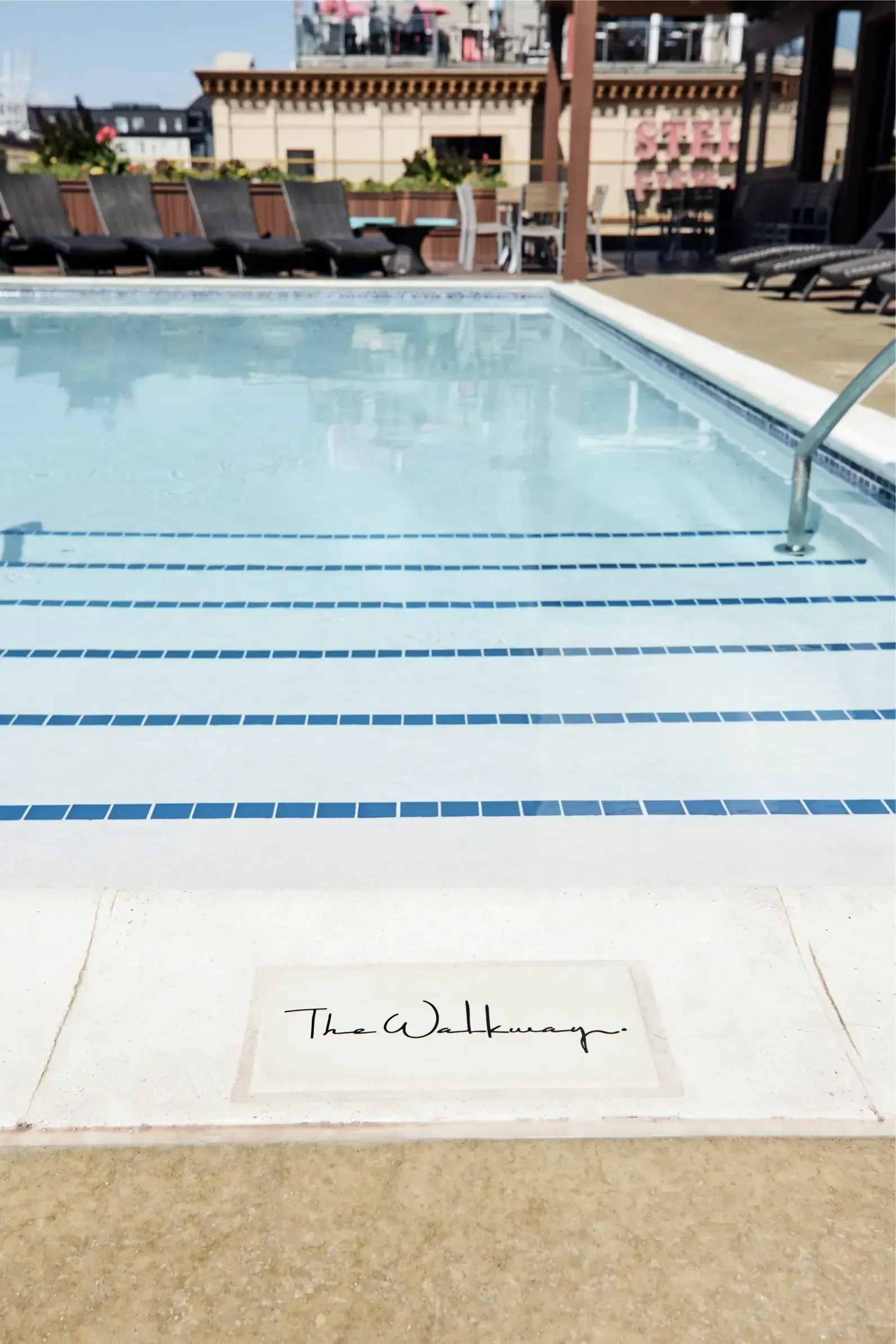 Outdoor pool area with blue-tiled steps, lounge chairs, and signage reading The Walkway on the deck.