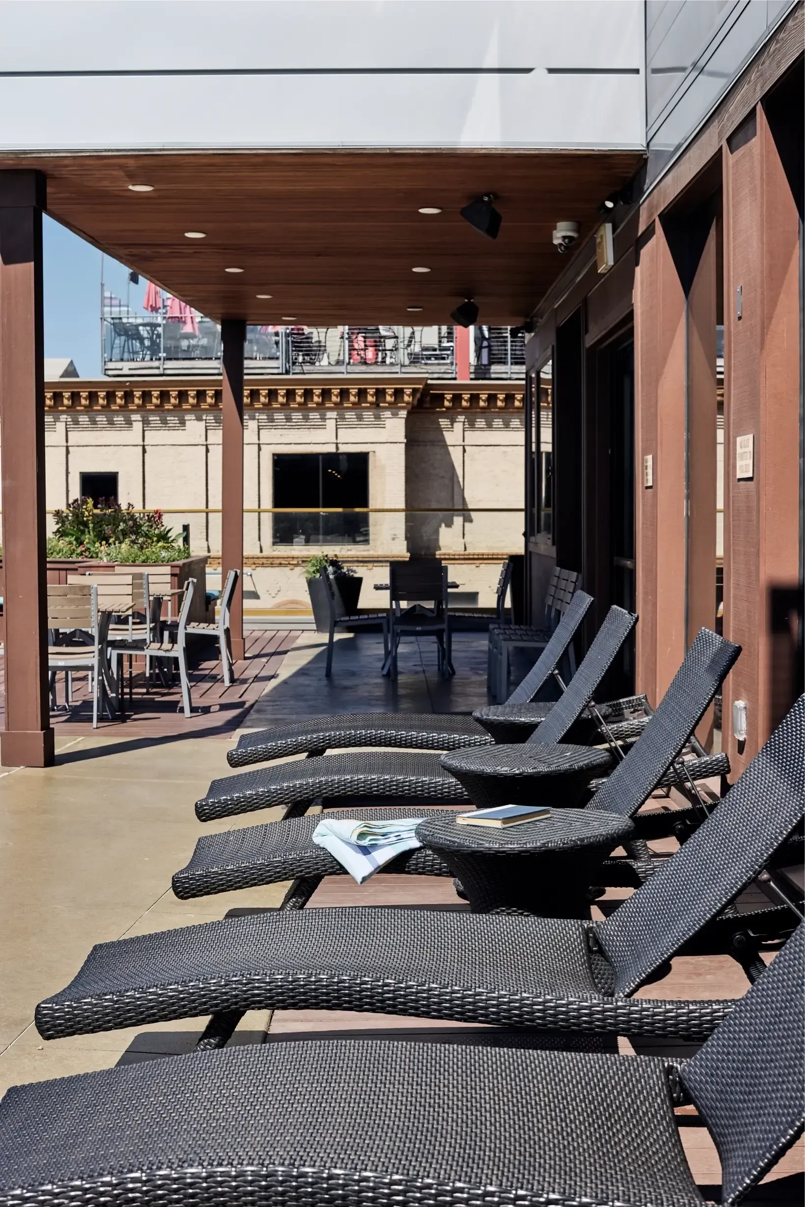 Outdoor amenity deck with wicker lounge chairs and tables under a wood-paneled ceiling.
