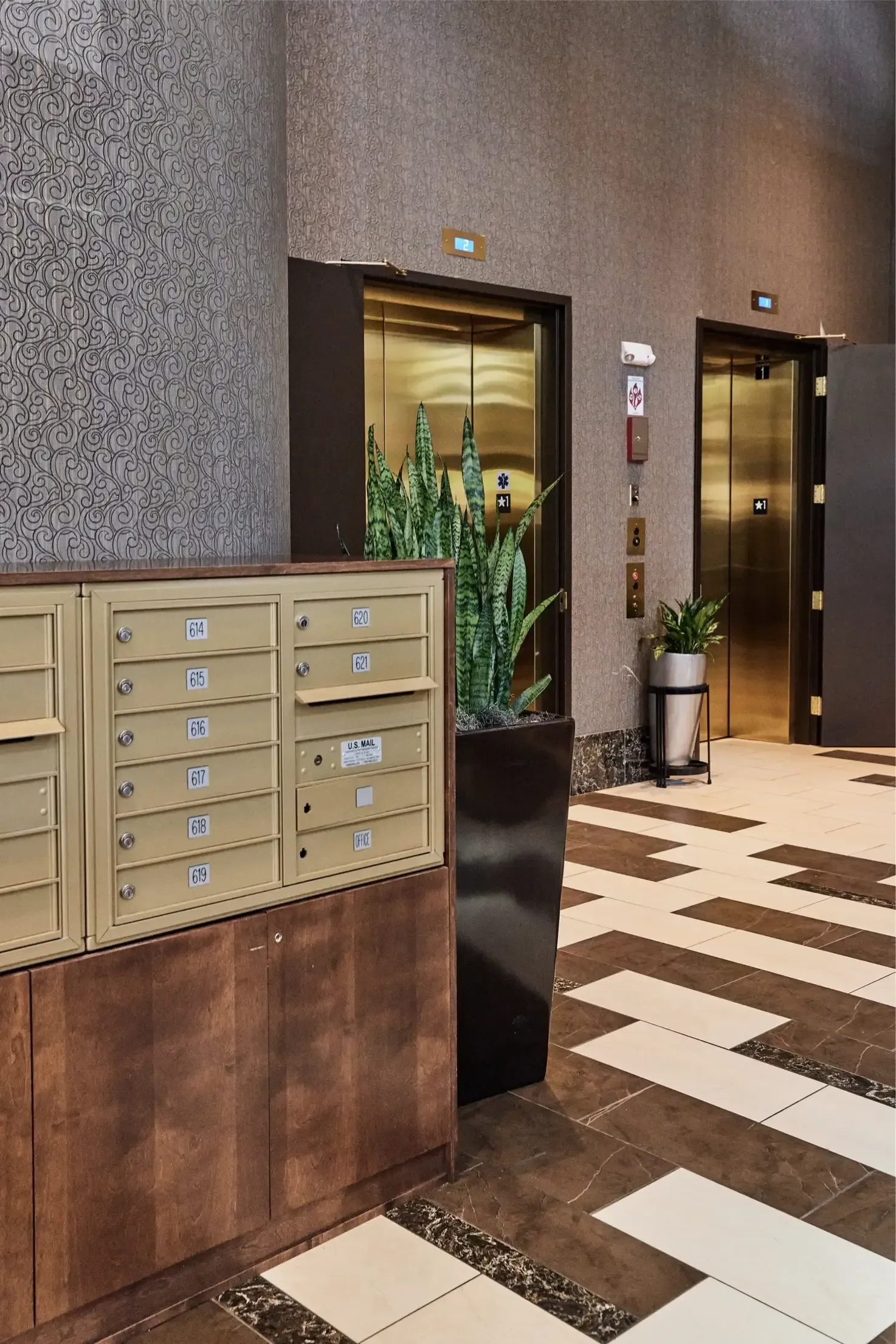 Lobby with beige mailboxes, two elevators, and potted plants.