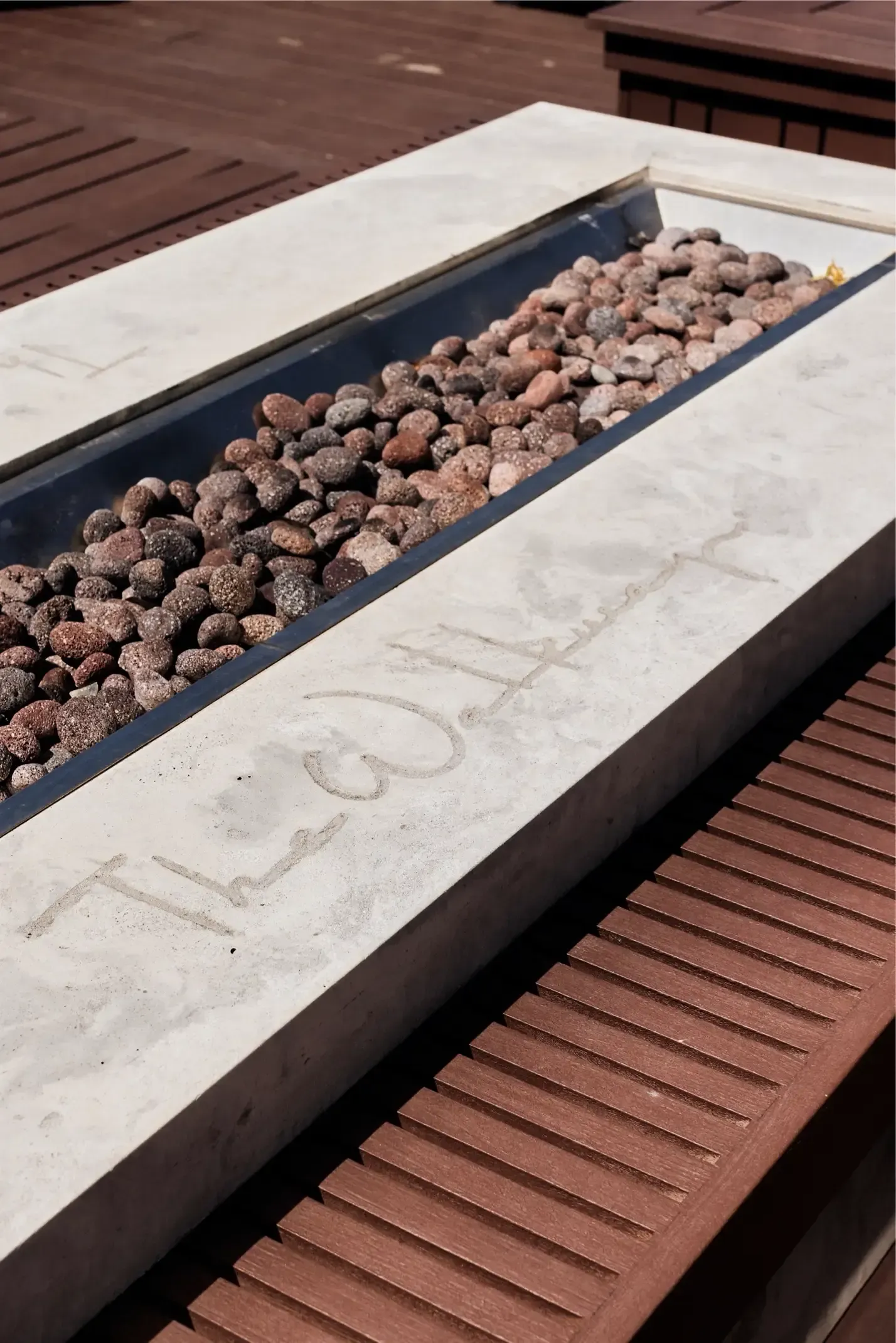 Concrete planter filled with brown pebbles on a wooden deck.