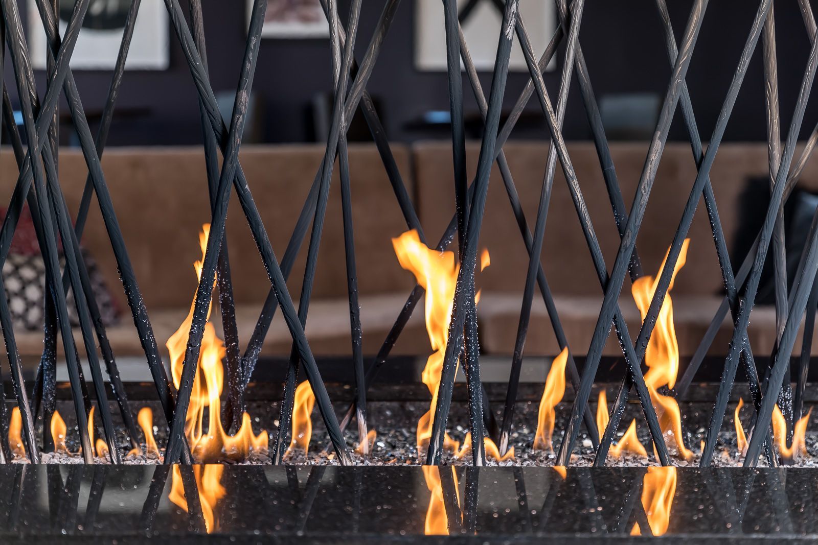 Outdoor fire pit with crisscross metal rods and dancing flames; seating blurred in the background.
