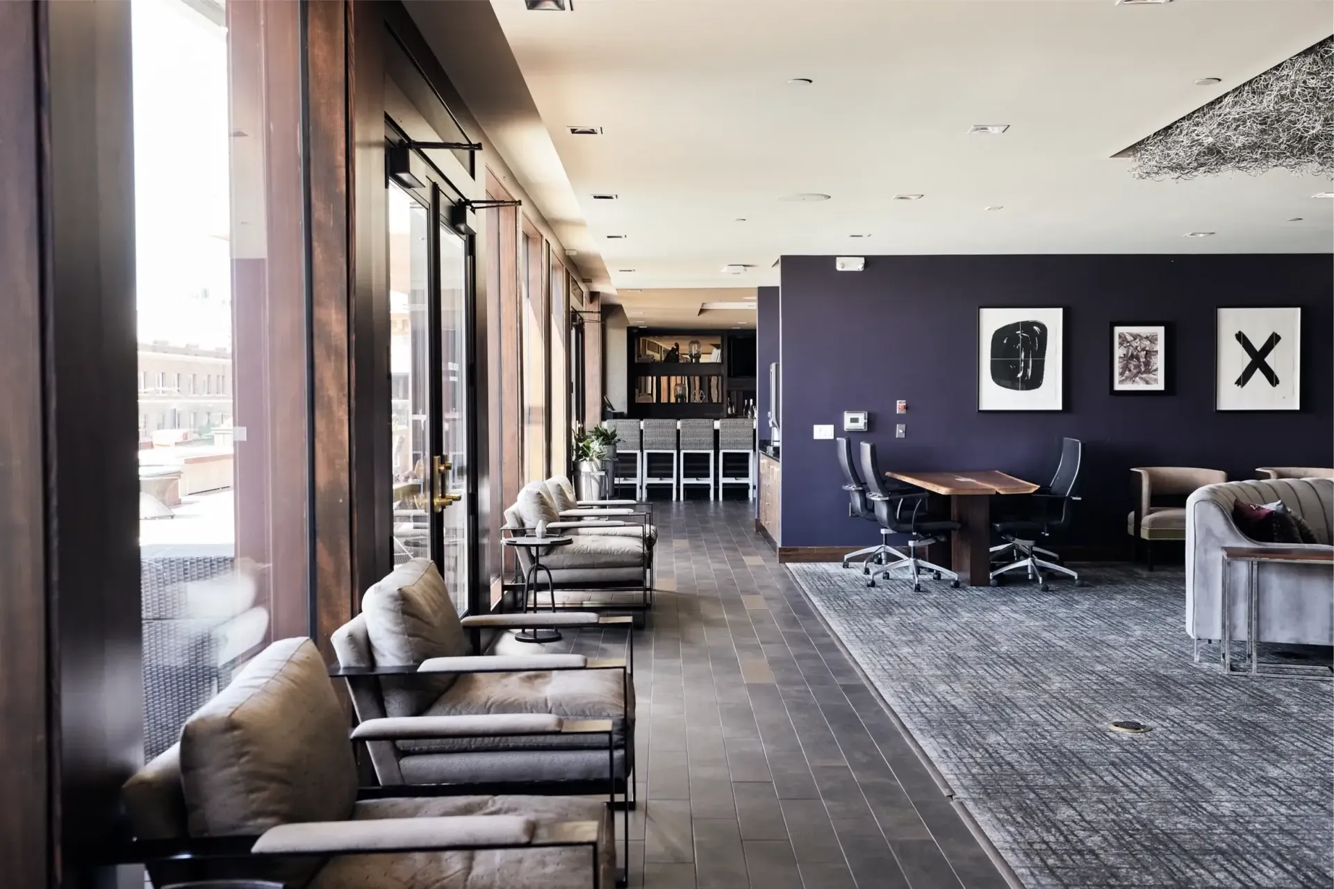 Lobby seating along floor-to-ceiling windows with armchairs and a dark purple accent wall.