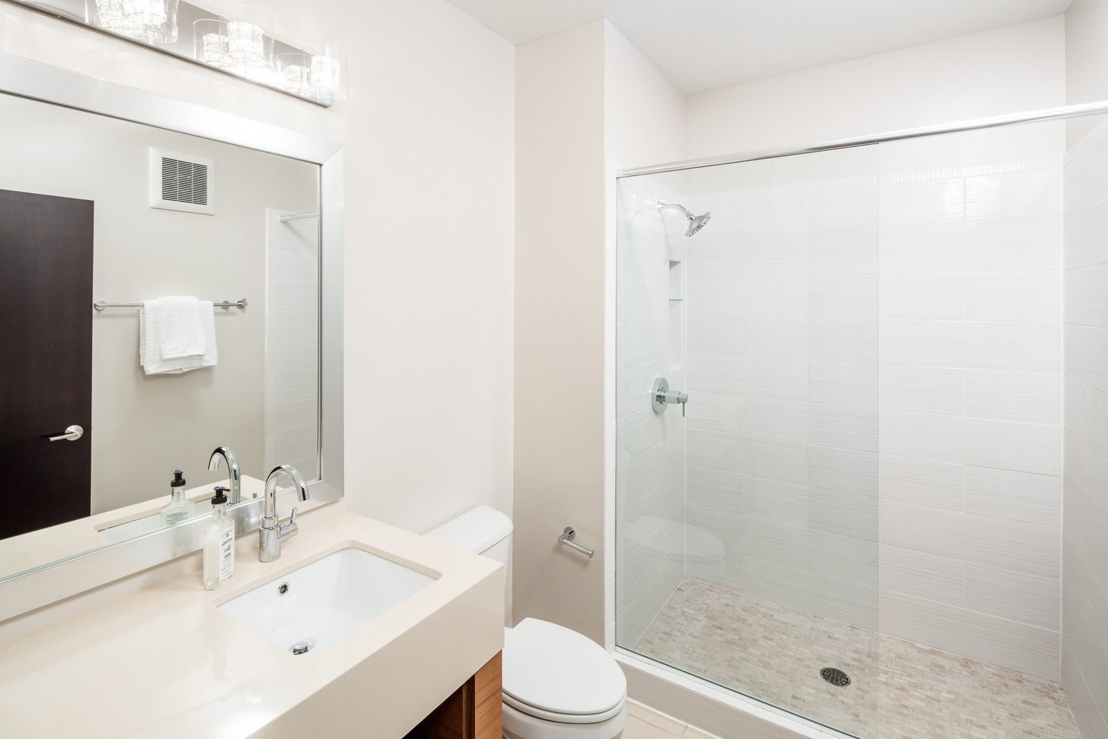 Modern apartment bathroom with sink, toilet, and glass-enclosed shower.