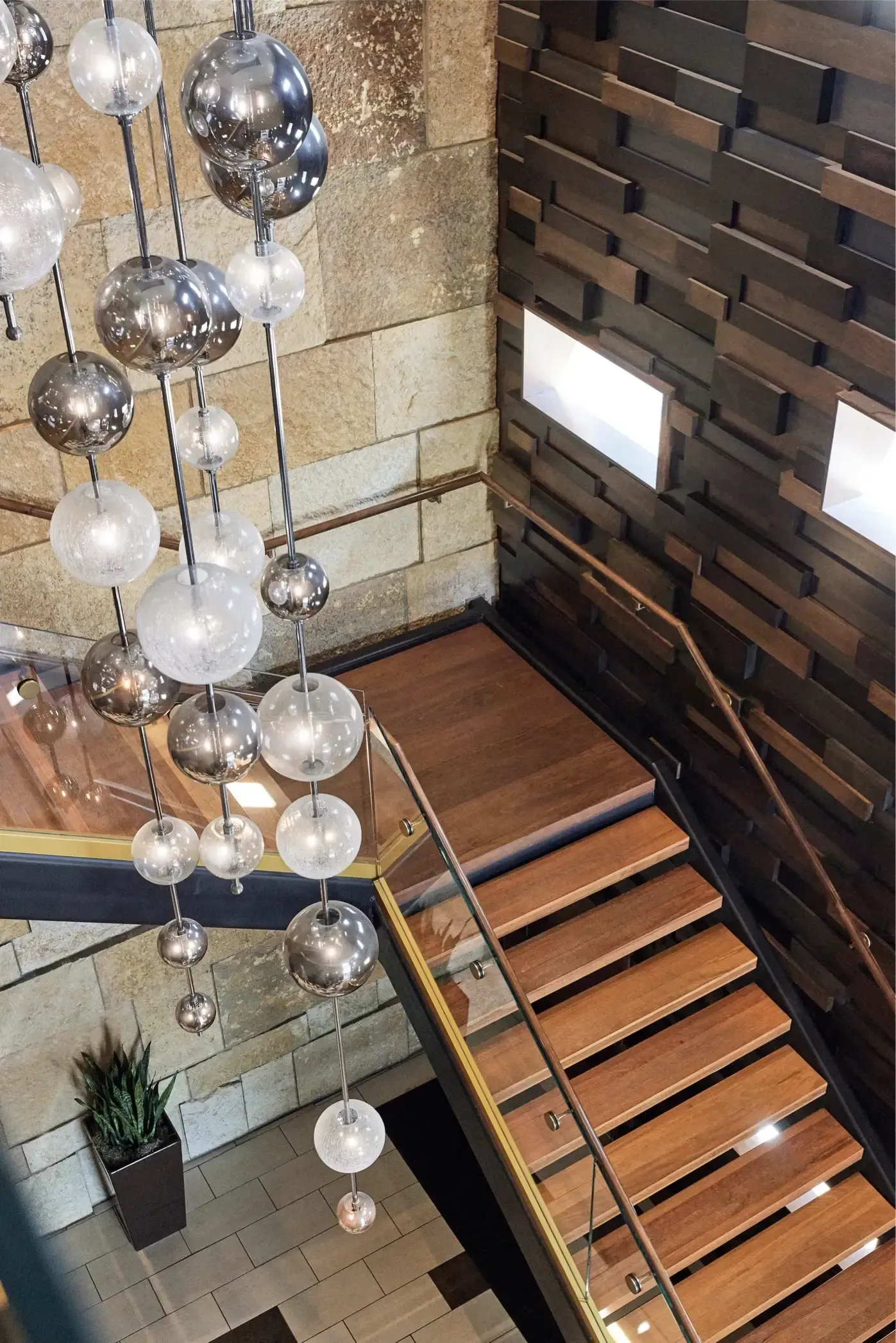 Interior staircase in a modern building lobby with glass railing and hanging spherical chandelier.