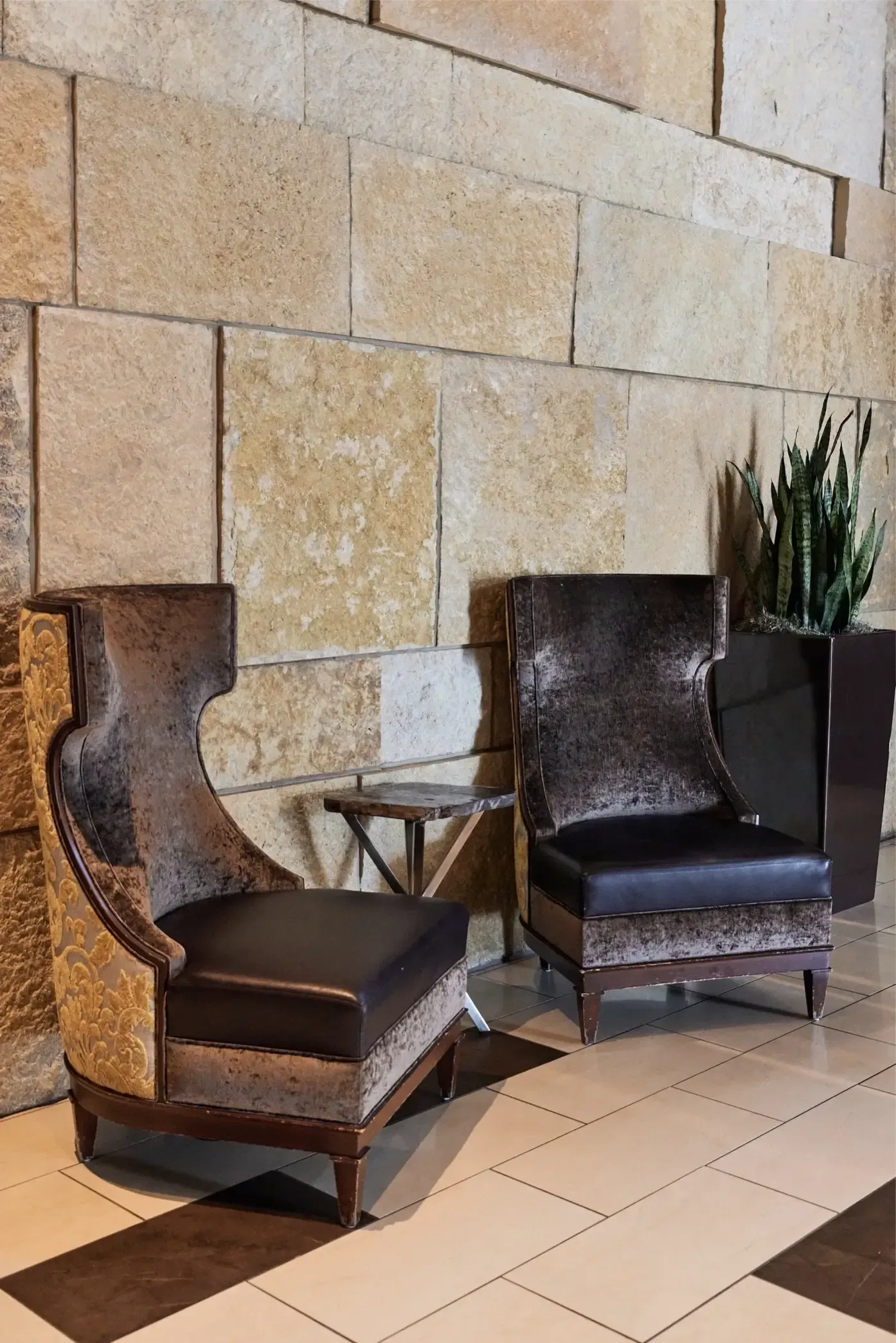 Two dark upholstered lounge chairs with a small side table in a stone-walled lobby.