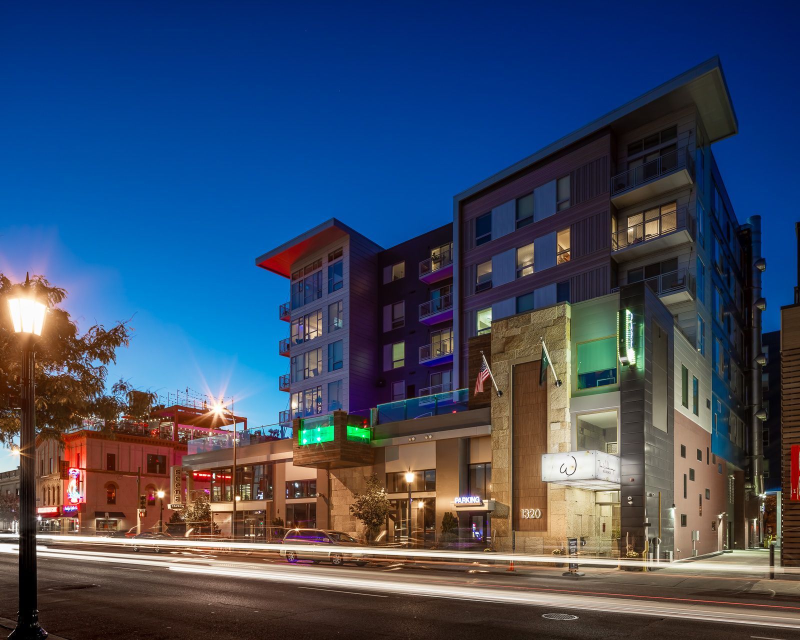 Nighttime exterior view of a modern apartment building with lit storefronts and street.