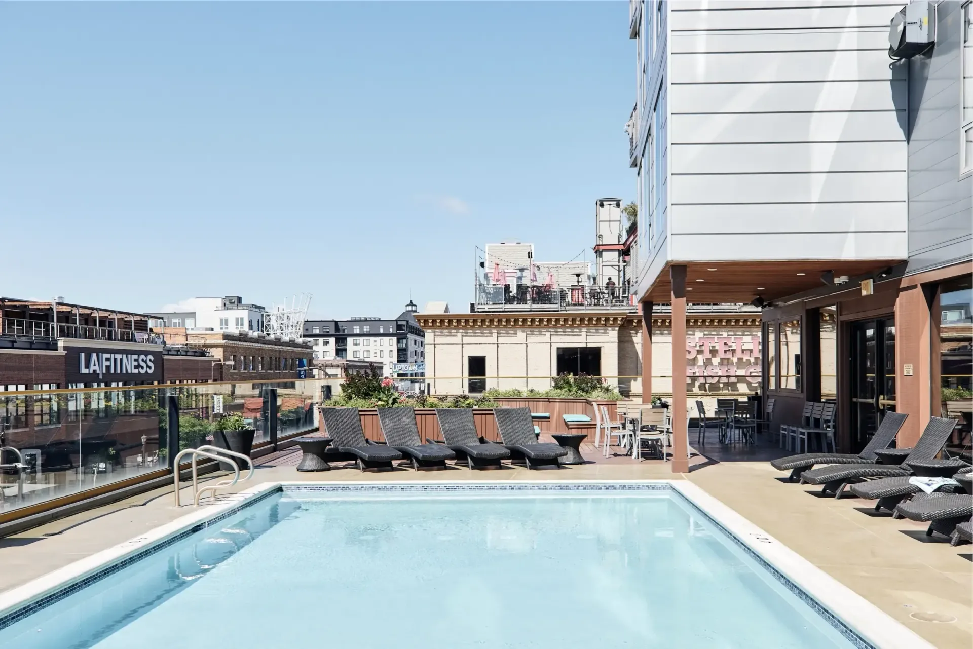 Rooftop pool with lounge chairs and patio seating on a sunny day.