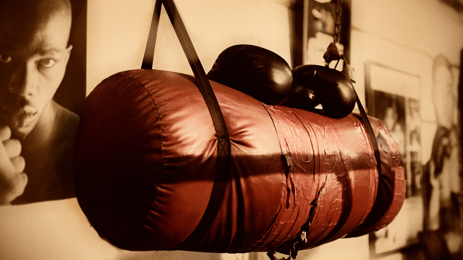 A boxing bag is hanging on a wall next to a picture of a boxer.