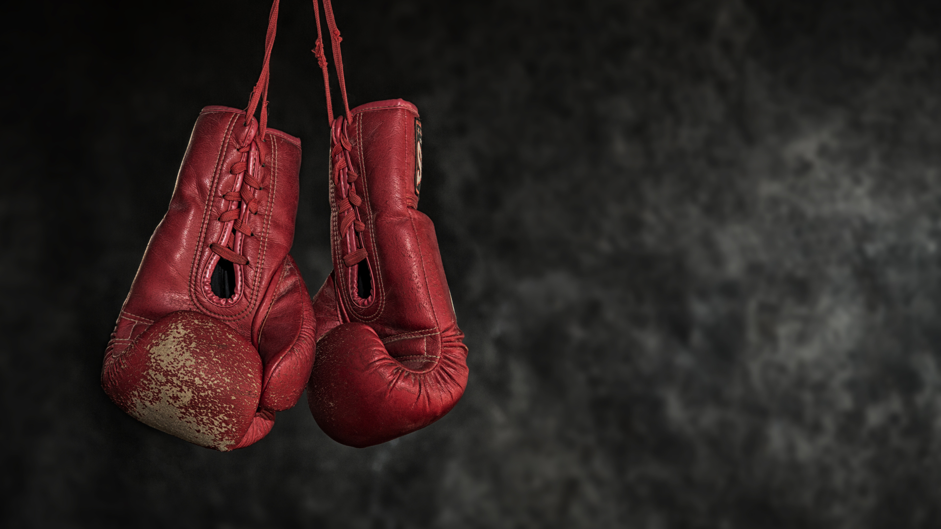 A pair of red boxing gloves hanging from a string on a black background.