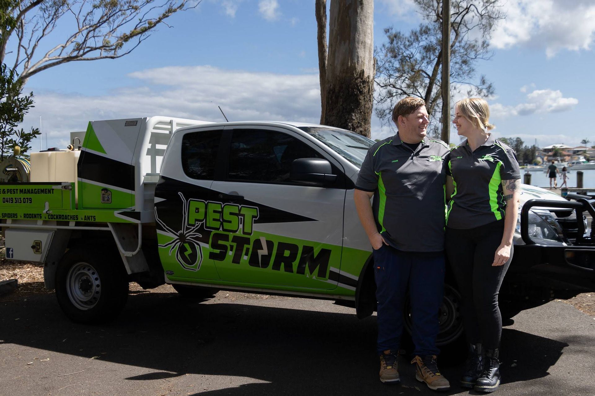 Two People Stand Smiling Next to a White Service Truck — Pest Storm In Summerland Point, NSW
