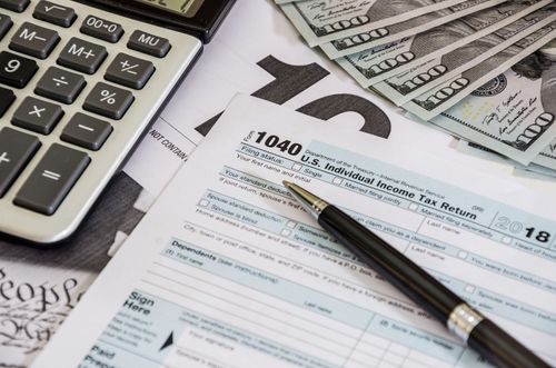 Calculator, pen, and IRS Form 1040 on papers with money, suggesting tax preparation